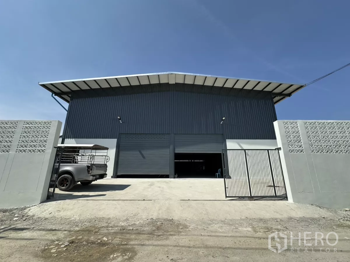 货栈 出租在Prawet, Bangkok - 仓库正立面，金属外墙、宽幅卷闸门与门禁入口，前方装卸坪，曼谷Prawet。