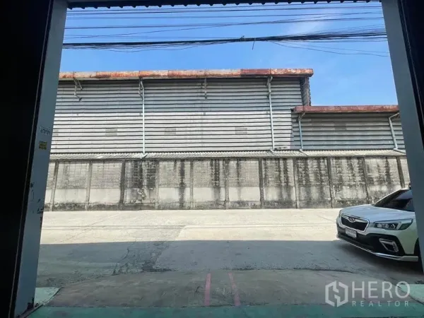 Warehouse for rent in Bang Phli, Samut Prakan - View from the warehouse loading bay to a wide driveway with a parked car and neighboring industrial building.