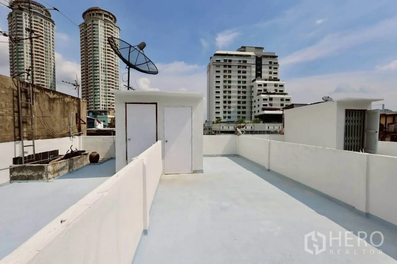 Shophouse for rent in Sathon, Bangkok - Rooftop terrace with satellite dish and storage rooms, city buildings beyond.