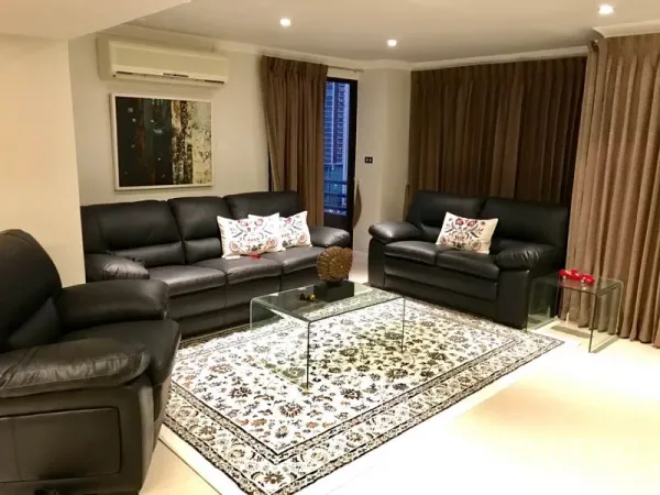 Condominium for rent in Bang Rak, Bangkok - Contemporary living room with black leather sofas, glass coffee table and patterned rug.