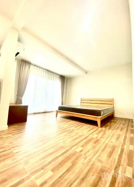 Townhouse for rent in Prawet, Bangkok - Bright bedroom with bed, sheer curtains and wood flooring.