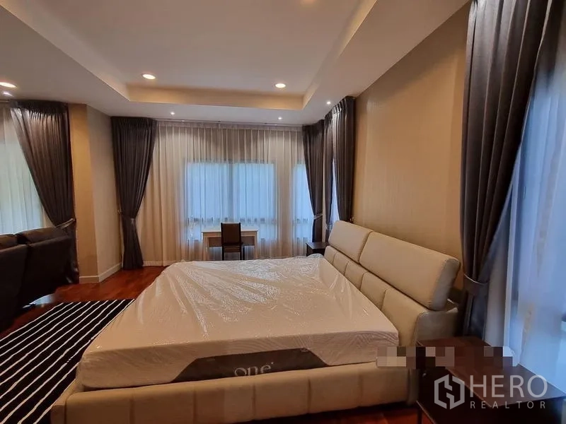 Detached House for rent in Bang Khae, Bangkok - Spacious master bedroom with large bed, wood floors, recessed lighting and full-length curtains.