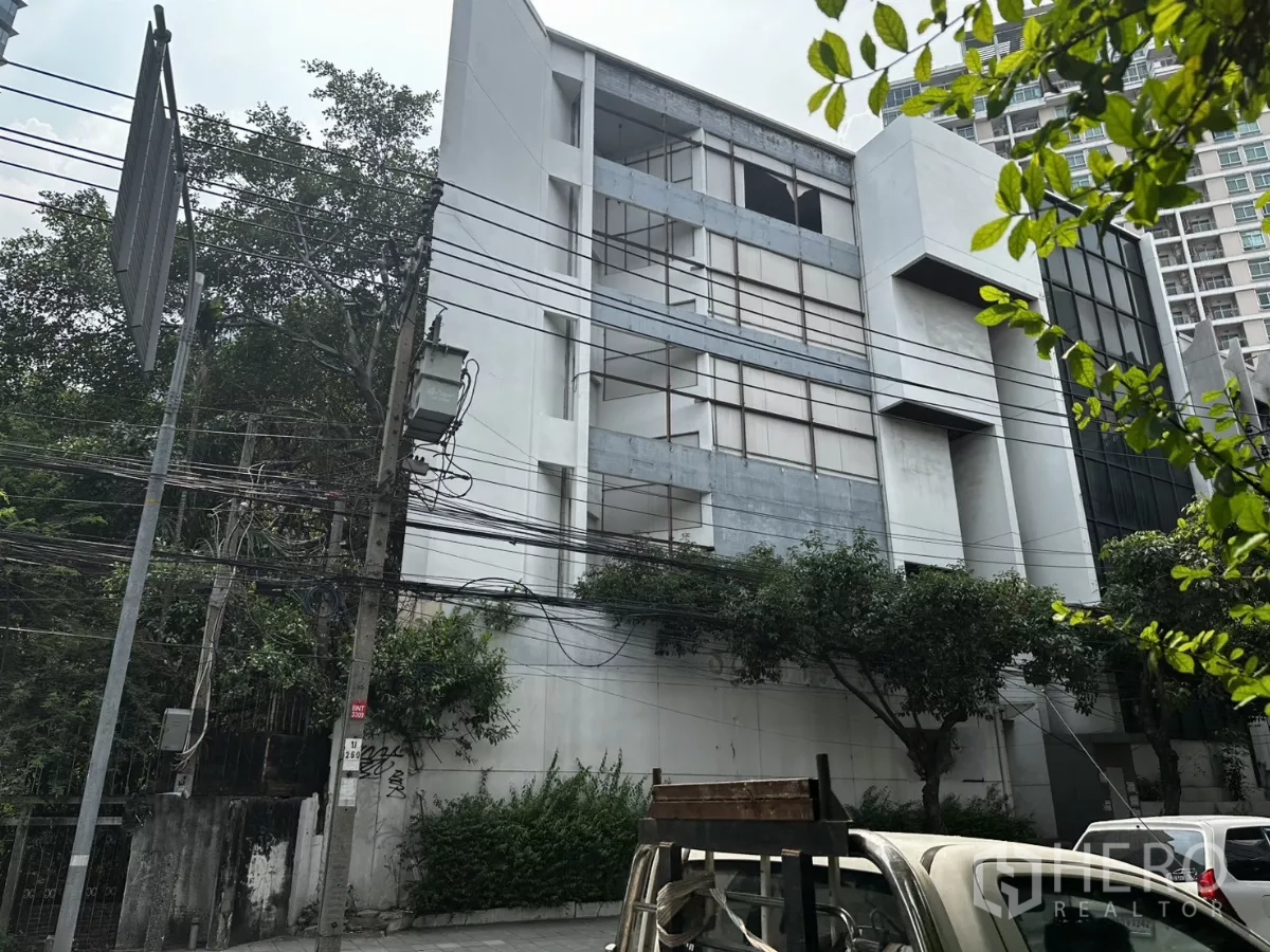 零售空间 出租在Bang Na, Bangkok - 邦那素坤逸路临街多层商业楼，立面宽阔，前方有树木与电线。