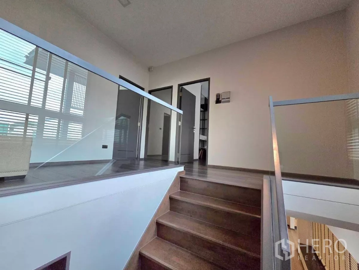 Detached House for rent in Bang Phli, Samut Prakan - Upper-floor landing with wood stairs and clear glass balustrades filled with natural light.