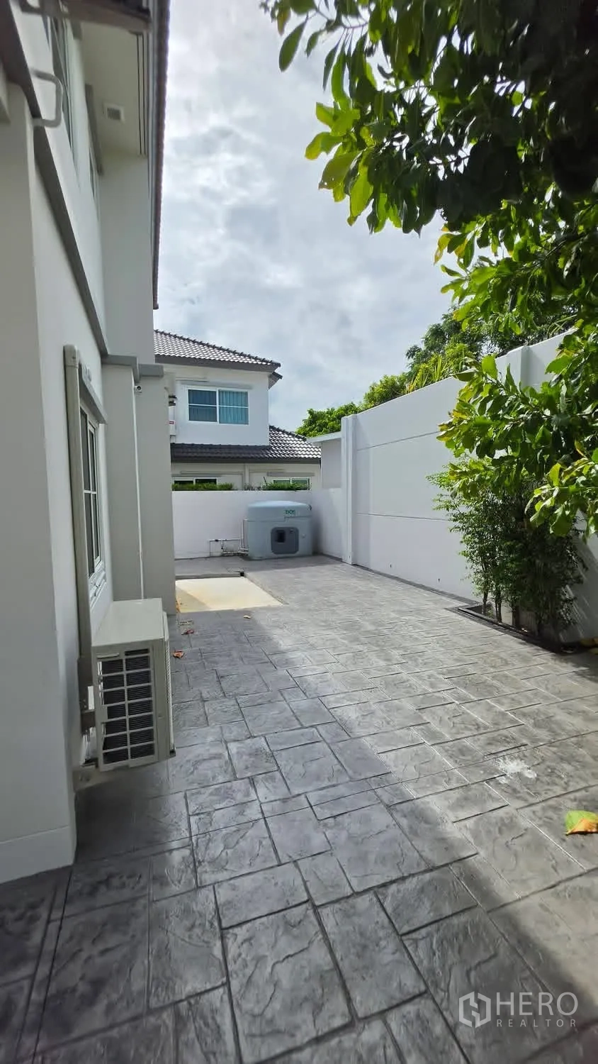Detached House for rent in Bang Phli, Samut Prakan - Spacious paved backyard with privacy walls, tree shade, and a utility water tank.