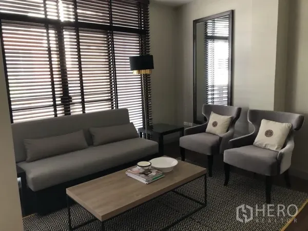 อพาร์ทเมนท์ ให้เช่าในKhlong Toei, Bangkok - มุมนั่งเล่นอีกห้องพร้อมโซฟาสีเทา เก้าอี้อาร์มแชร์ โต๊ะกลาง โคมไฟ และหน้าต่างบานใหญ่พร้อมมู่ลี่ไม้