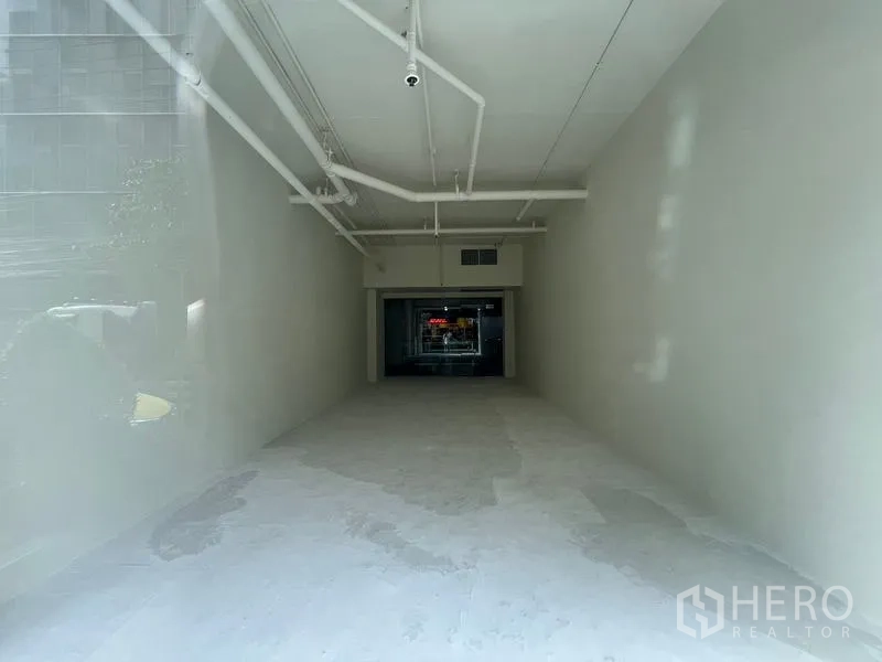 零售空间 出租在Watthana, Bangkok - 狭长店铺内部，外露管线与通往商场的玻璃门。