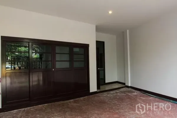 Townhouse for rent in Khlong Toei, Bangkok - Covered carport and entry area with dark wood sliding doors and tiled floor.