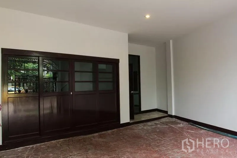 Townhouse for rent in Khlong Toei, Bangkok - Covered carport and entry area with dark wood sliding doors and tiled floor.