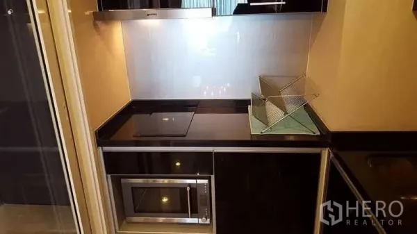 Condominium for rent in Khlong Toei, Bangkok - Compact black-and-white kitchen with induction hob, hood and built-in microwave.