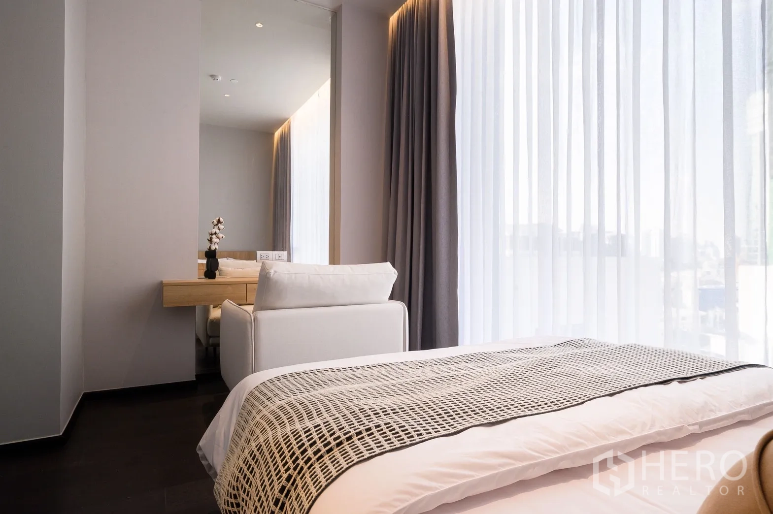 Condominium for rent or sale in Watthana, Bangkok - Sunlit bedroom corner with full-height curtains, vanity desk and neutral decor.