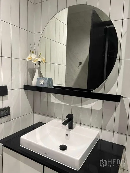 คอนโด ให้เช่าในKhlong San, Bangkok - เคาน์เตอร์อ่างล้างหน้าในห้องน้ำ กระจกกลม ท็อปสีดำ และอ่างทรงสี่เหลี่ยมบนผนังกระเบื้องสีขาว