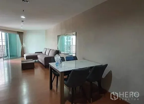 Condominium for rent in Huai Khwang, Bangkok - Open-plan living and dining space with a marble-top table and sliding door to a balcony with curtains.