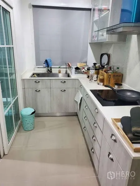 Detached House for sale in Bueng Kum, Bangkok - Compact enclosed kitchen with L-shaped counter, induction hob and light wood cabinets.
