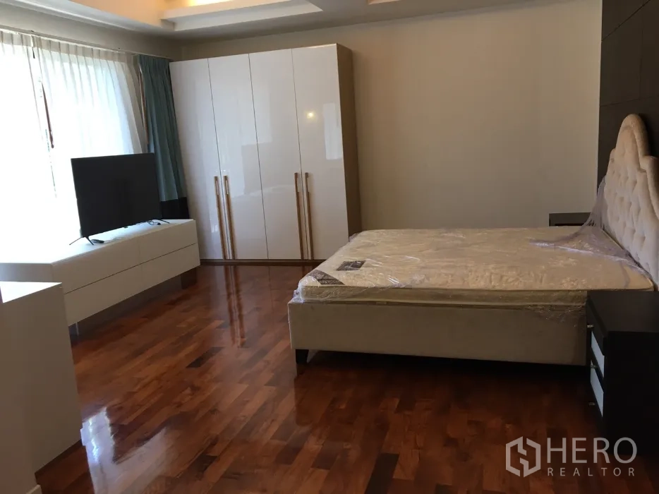 Detached House for rent in Watthana, Bangkok - Spacious master bedroom with glossy wood floors, large wardrobe, TV stand and upholstered bed.