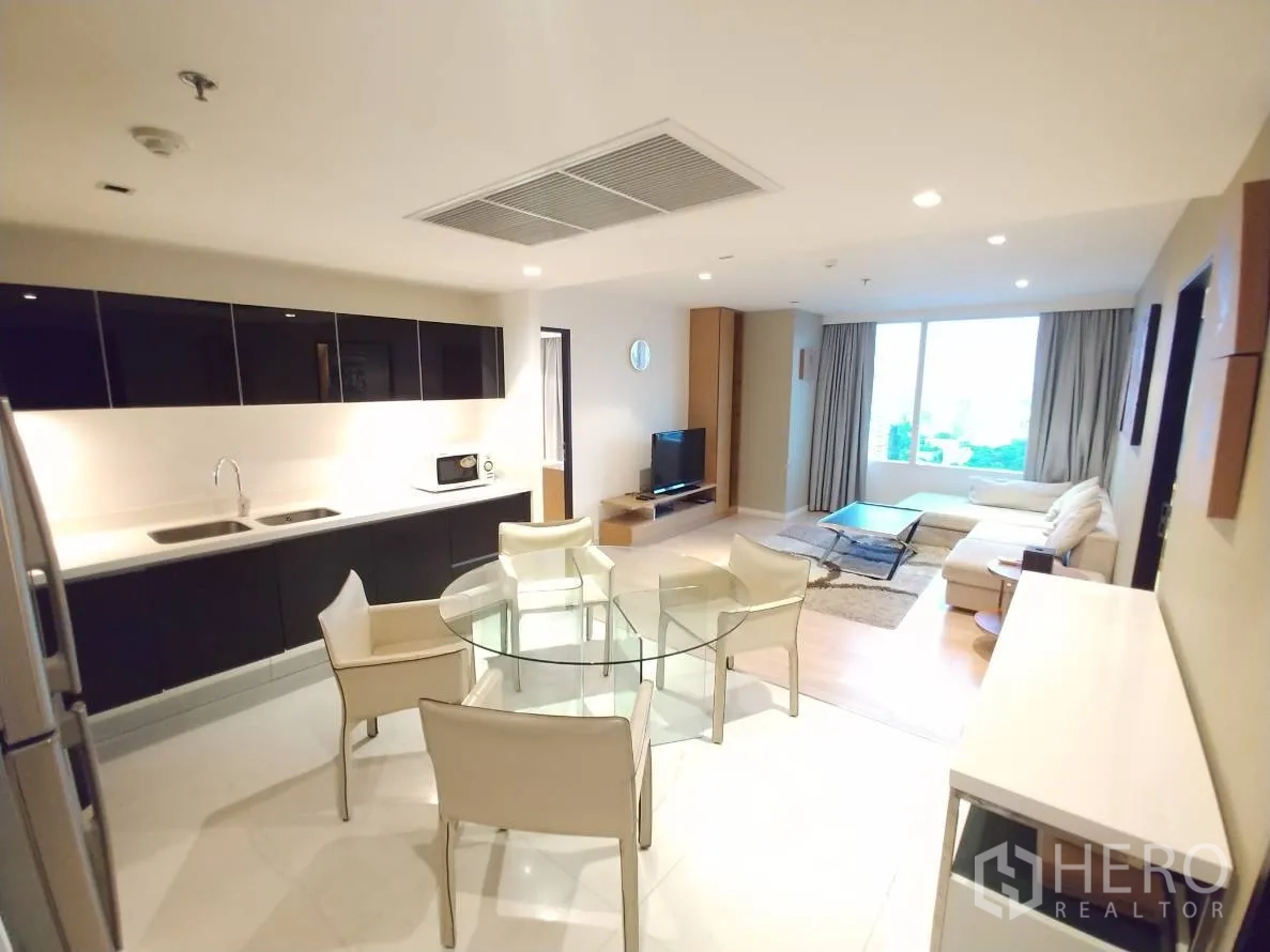 公寓 出租在Watthana, Bangkok - 开放式客餐厨，线性橱柜、双槽水槽、玻璃圆餐桌与浅色沙发。