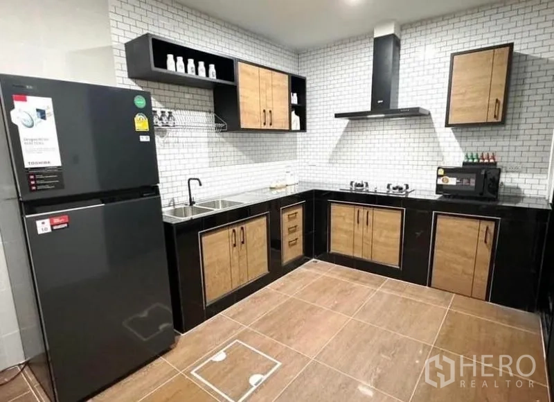 Townhouse for rent - L-shaped kitchen with white subway tiles, black countertops, wood cabinets, and large fridge.