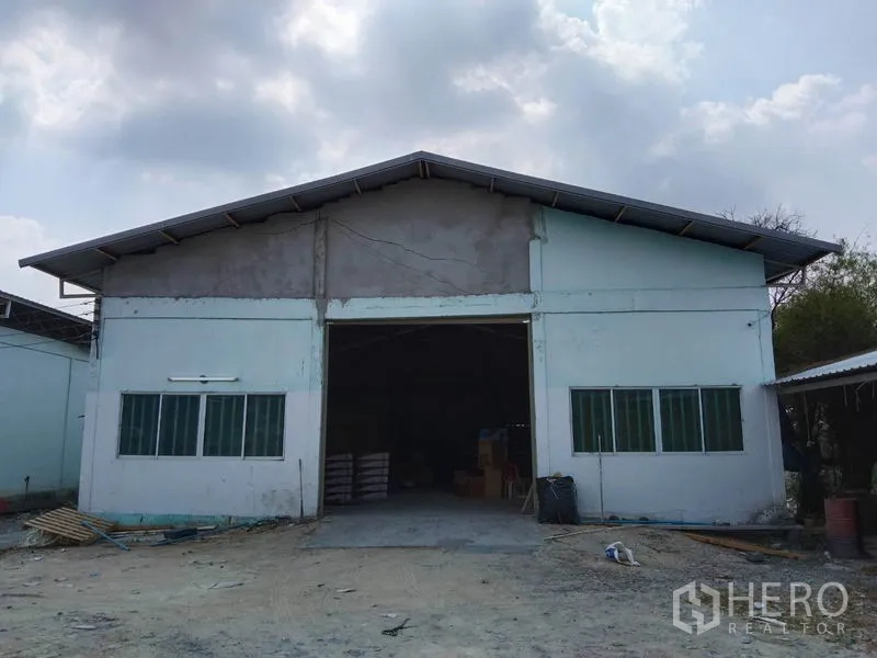 Warehouse for rent in Khlong Sam Wa, Bangkok - Front exterior of a gable‑roof warehouse with wide loading entrance and side windows in Khlong Sam Wa, Bangkok.