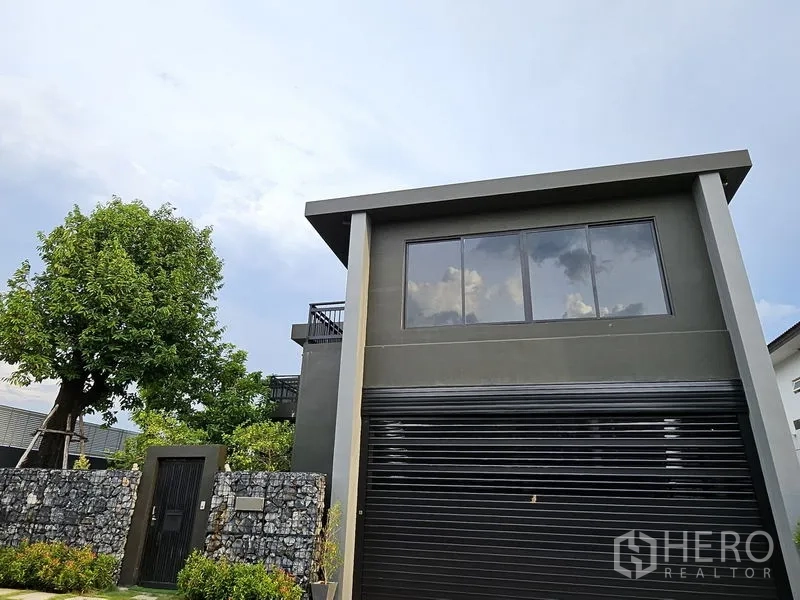 Detached House for sale in Thawi Watthana, Bangkok - Angled view showing balcony, expansive glazing and landscaped frontage.
