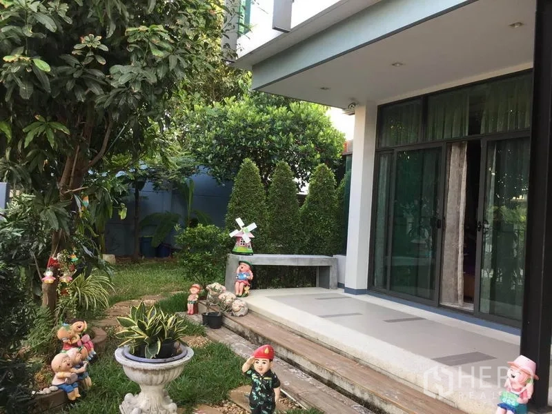 Detached House for sale in Pak Kret, Nonthaburi - Front porch and lawn garden with sliding glass doors, a bench and decorative statues.