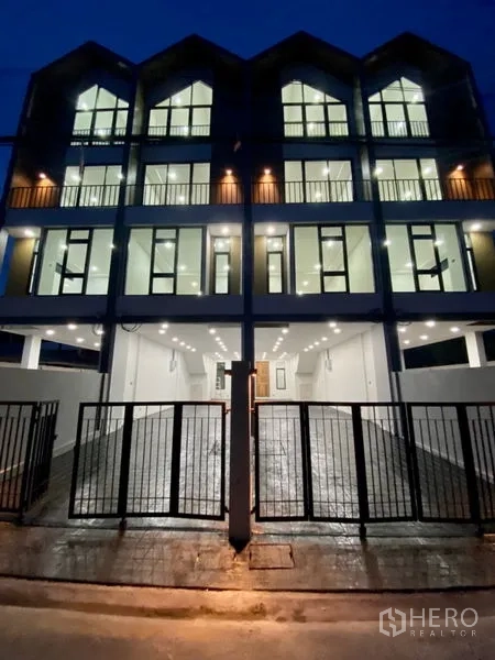 带办公室的家 出租或出售在Bang Na, Bangkok - 夜景外观，四层住办公楼灯光通明，带大门的车道。