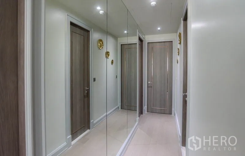 Condominium for rent or sale in Watthana, Bangkok - Hallway with mirrored wall, wood doors and recessed lighting.