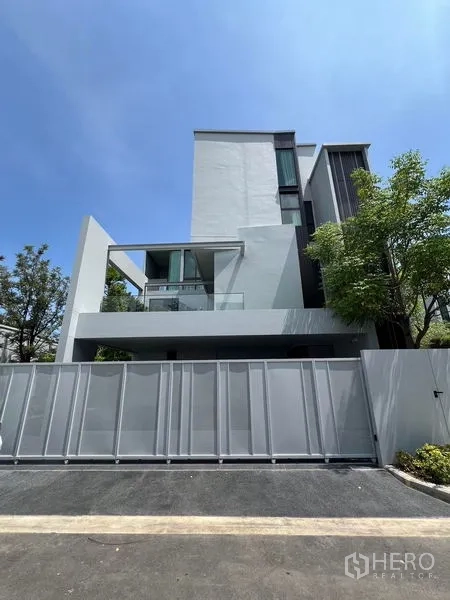 Detached House for rent in Saphan Sung, Bangkok - Street-side view of a modern multi-level detached house with high fence and trees.