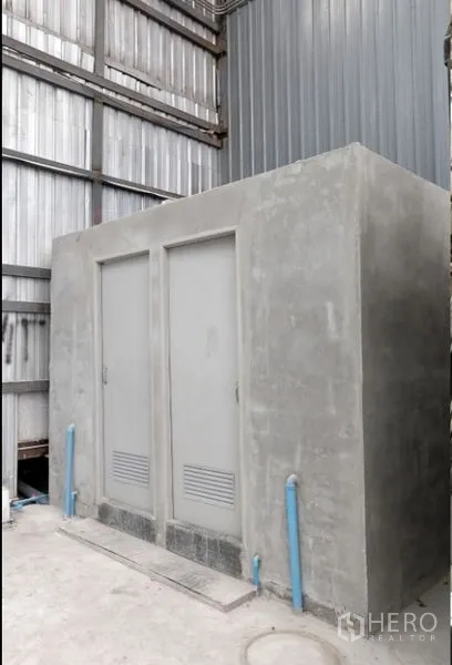 Warehouse for rent in Pak Kret, Nonthaburi - Concrete restroom block with two doors and visible plumbing inside the warehouse.
