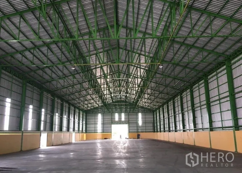 Warehouse for rent in Mueang Samut Songkhram, Samut Songkhram - Open warehouse interior with high gabled roof, green steel trusses, side windows and polished concrete floor.