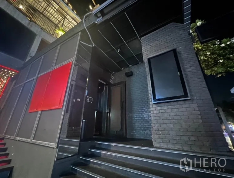 零售空间 出租在Bangkok - 夜间深色砖墙外立面，带雨棚和台阶的商铺入口