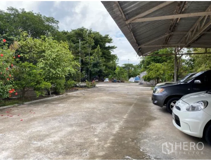 Land for sale in Lat Krabang, Bangkok - Covered parking area with cars and surrounding trees on a spacious concrete yard.
