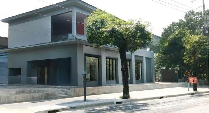 零售空间 出租在Khlong Toei, Bangkok - 转角灰色商铺立面，高挑落地窗，临街绿树与人行道。