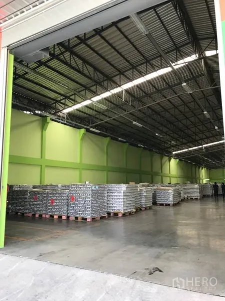 货栈 出租在Ban Phaeo, Samut Sakhon - 卷帘门开启的仓库入口，内部高挑空间与堆放的托盘货物。