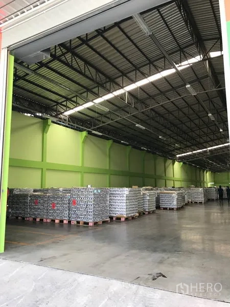 货栈 出租在Ban Phaeo, Samut Sakhon - 卷帘门开启的仓库入口，内部高挑空间与堆放的托盘货物。