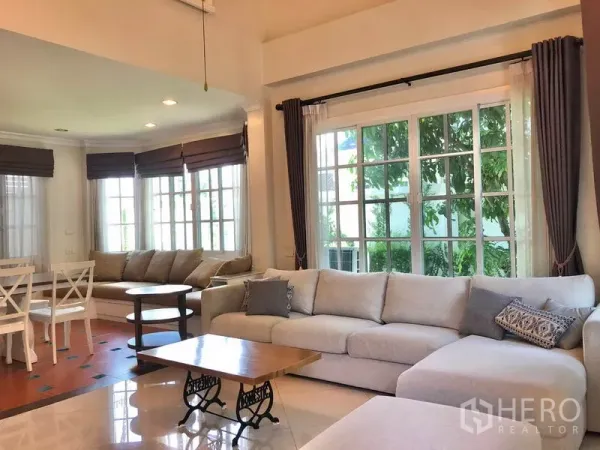 独立式住宅 出租在Mueang Samut Prakan, Samut Prakan - 明亮客厅，转角沙发、大面积窗户、窗帘与茶几