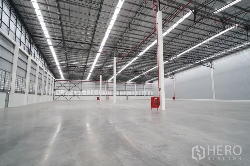 Warehouse for rent in Khlong Luang, Pathum Thani - High-ceiling warehouse interior showing sprinkler piping, support columns, and smooth concrete flooring.