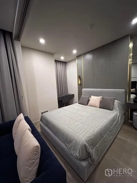 Condominium for rent in Watthana, Bangkok - Cozy bedroom with upholstered bed, textured feature wall, and soft lighting.