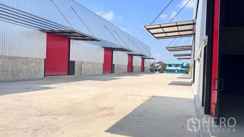 货栈 出租在Khlong Sam Wa, Bangkok - 宽阔混凝土场地，多个红色卷帘装卸门与带雨棚的装卸区。