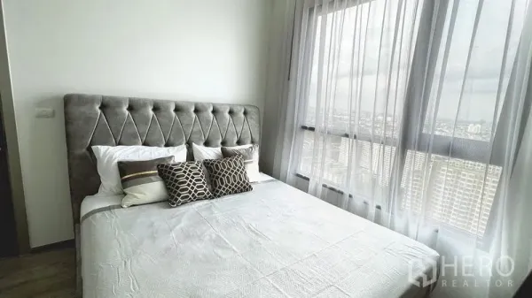 Condominium for rent in Watthana, Bangkok - Master bedroom with tufted headboard, sheer curtains, and expansive city view from tall windows.