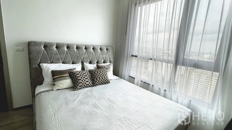Condominium for rent in Watthana, Bangkok - Master bedroom with tufted headboard, sheer curtains, and expansive city view from tall windows.