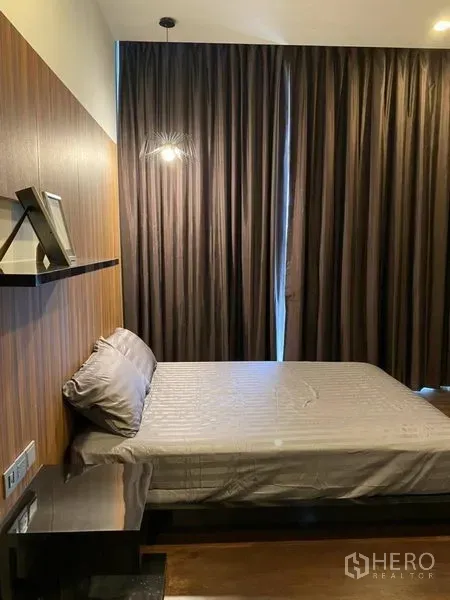 公寓 出租在Watthana, Bangkok - 卧室带木质背景墙、床侧置物架、柔和灯光与全遮光落地窗帘。