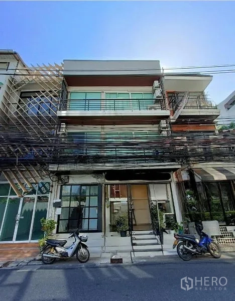 店屋 出售在Bang Rak, Bangkok - 四层临街店屋外立面，玻璃阳台与落地门面，门前停有摩托车。