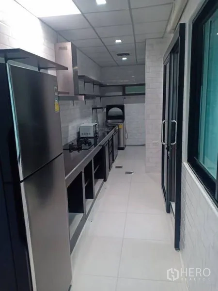 Detached House for rent in Thanyaburi, Pathum Thani - Enclosed Thai kitchen in a galley layout with gas hob, range hood, and stainless refrigerator.