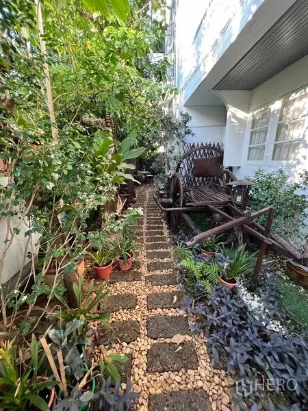 บ้าน ขายในLat Krabang, Bangkok - ทางเดินสวนร่มรื่น มีต้นไม้กระถางและเกวียนไม้ตกแต่งข้างบ้าน