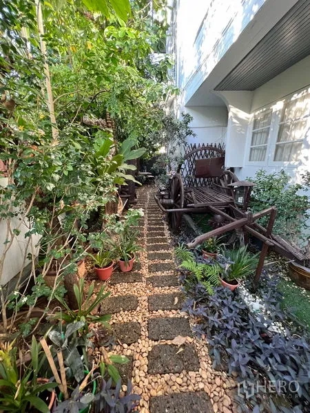 บ้าน ขายในLat Krabang, Bangkok - ทางเดินสวนร่มรื่น มีต้นไม้กระถางและเกวียนไม้ตกแต่งข้างบ้าน