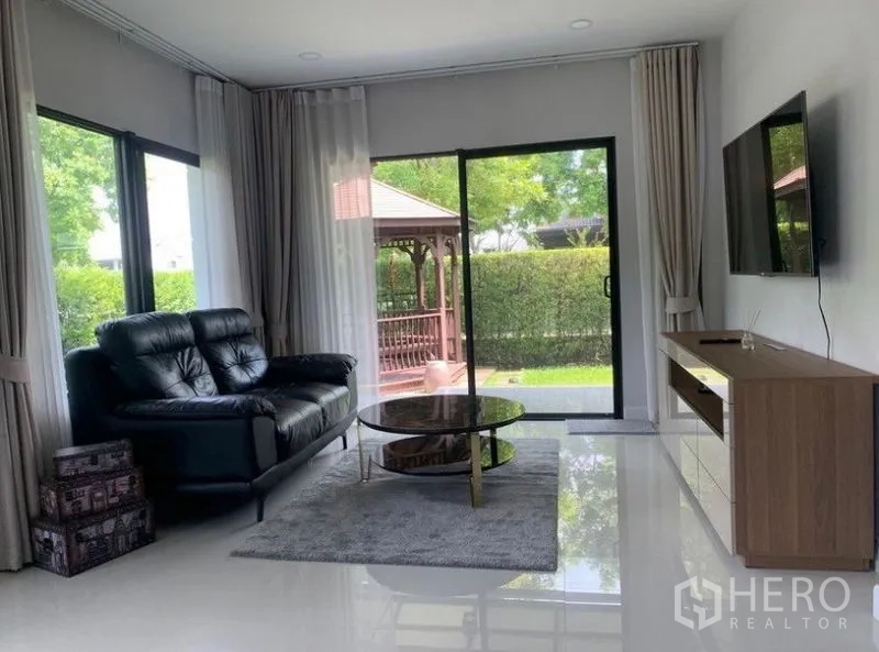 บ้าน ให้เช่าในPrawet, Bangkok - ห้องนั่งเล่นโซฟาหนัง ผนังทีวี ประตูกระจกเปิดออกสู่สนามหญ้าและศาลาไม้