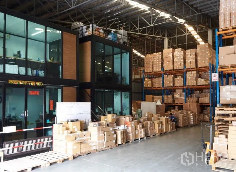 Warehouse for rent in Bang Na, Bangkok - High-ceiling warehouse interior featuring a glass-partitioned mezzanine office and tall pallet racking.