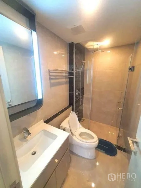 Condominium for rent or sale in Huai Khwang, Bangkok - Modern bathroom with glass-enclosed shower, illuminated mirror, and toilet.
