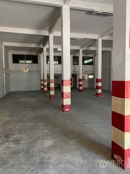 Warehouse for rent in Khlong Toei, Bangkok - Industrial floor with rows of red-banded pillars, side windows, and fluorescent lighting inside the warehouse.