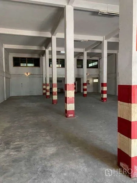 Warehouse for rent in Khlong Toei, Bangkok - Industrial floor with rows of red-banded pillars, side windows, and fluorescent lighting inside the warehouse.